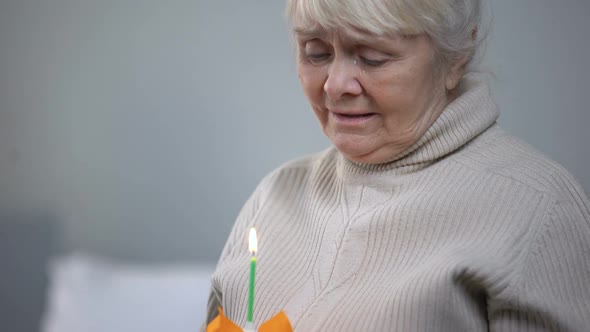 Crying Elderly Woman Blowing Out Candle on Birthday Cake, Loneliness in Old Age