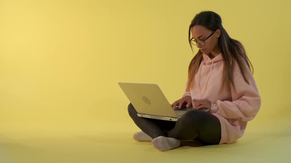 Smart African Girl Working on the Computer on Yellow Background