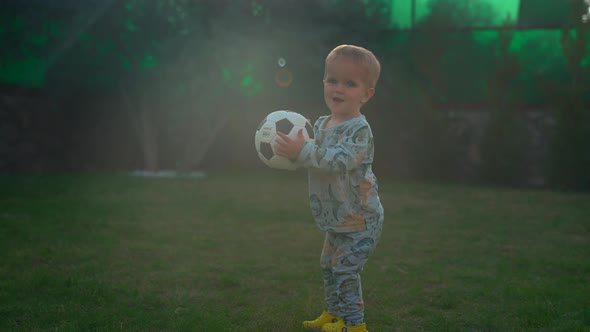 Cute Blond Boy Holds Soccer Ball Walking on Green Grass