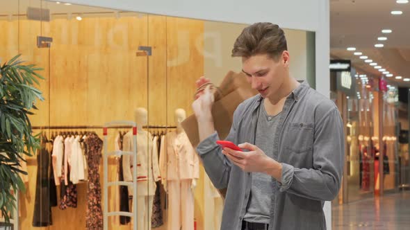 Young Man Smiling Using Smart Phone While Shopping at the Mall