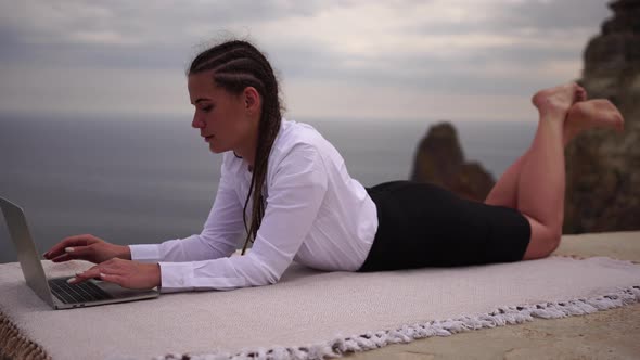 Well Looking Middle Aged Woman Typing on Laptop Keyboard Outdoors on Terrace with Beautiful Sea View