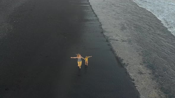 Aerial Shot of a Mother and Her Son Walking and Having Fun on a Beach with a Black Volcanic Sand