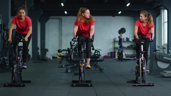 Group Athletic Girls Performing Aerobic Riding Training Exercises on Cycling Stationary Bike in Gym