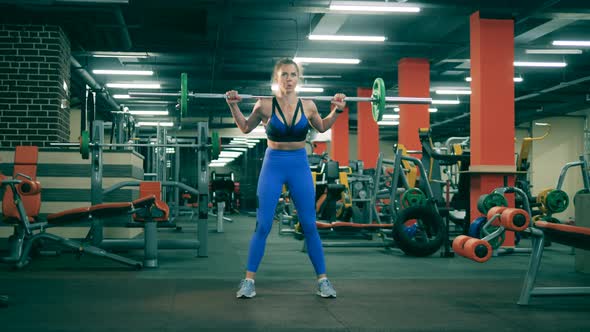 Sportswoman Squats with Barbell in Modern Gym.