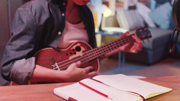 Female Asian Songwriter Playing the Guitar and Writing in Notepad