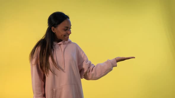 Beautiful African Woman Presenting Something on Empty Hand with Yellow Background.