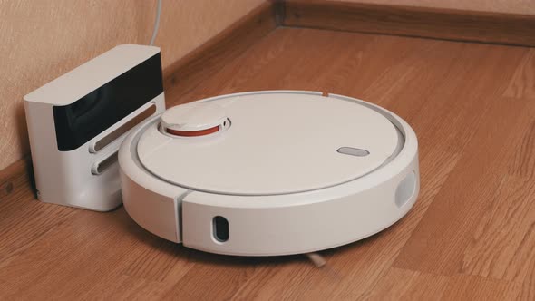 White Robotic Vacuum Cleaner Finishes Cleaning And Drives to Its Charging Station