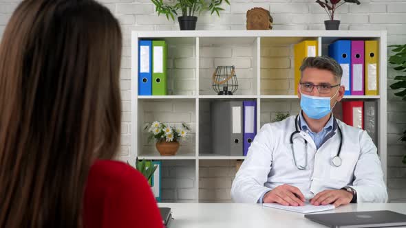 Doctor in mask consults speaks listens patient, client tells symptoms disease