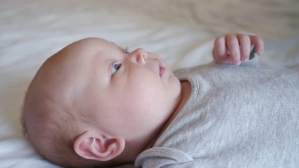 Sweet Newborn Girl Waves Hands Looking at Parent in Bedroom