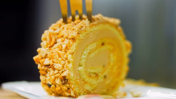 The Woman Takes a Piece of Cake Rolled with Peanuts with a Gold Fork