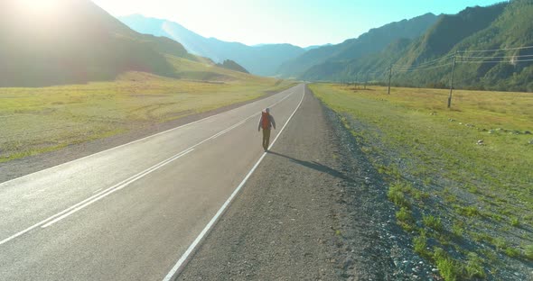 Flight Over Hitchhiker Tourist Walking on Asphalt Road. Huge Rural Valley at Summer Day. Backpack