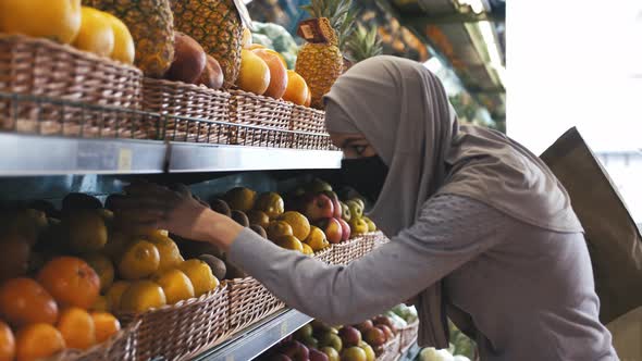 Close Up Shot of Young Beautiful Muslim Woman in Hijab and Protective Mask Choosing Fruits in the