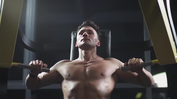 Athletic Man in the Gym Lifting Blocks on Gym Machine Training on Block Device Night Training