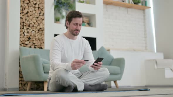 Young Man Making Online Payment on Smartphone on Yoga Mat