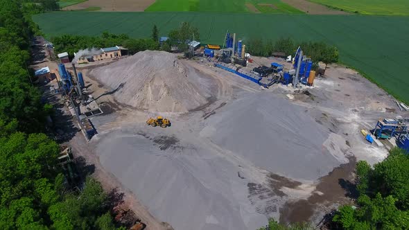 Territory of a mobile asphalt plant. Smoke from the enterprise chimney and embankments of rubble