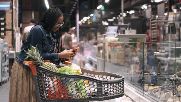 African Amercan Girl with Phone and Trolley in a Supermarket