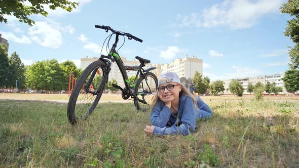 12 Year Old Girl Lying on the Grass Next To Her Bike and Smiling