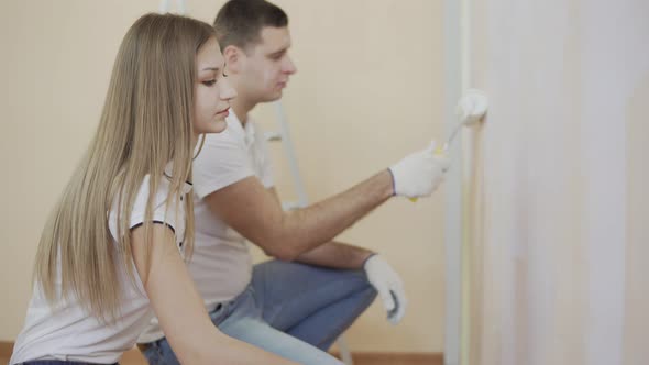 Young Couple in White Shirts Decorate Their New Apartment and Painting the Wall Using Paint Rollers