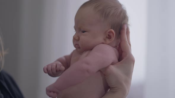 Side View Little Infant in Female Caucasian Hands Indoors at Home