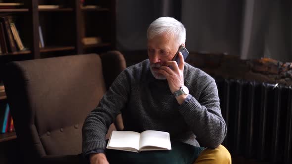 Serious Handsome Gray-haired Mature Man Talking on Cell Phone and Taking Notes in Paper Documents.