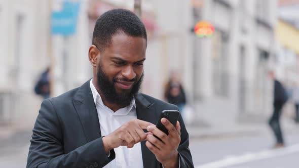 Smiling Young Biracial Black Man Holding Smartphone Looking at Phone Screen Look for Address with