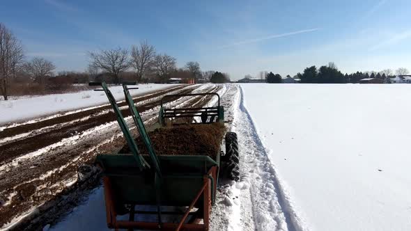 Agricultural Machinery Is Being Pulled To Spread Manure On Farmland During Sunny Winter Day. - Track