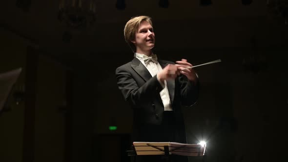 conductor leads the orchestra in a dark hall