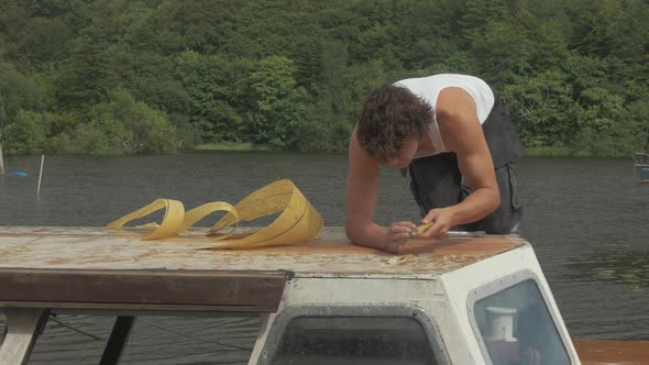 Carpenter res old epoxy fiberglass resin on cabin roof planking wooden boat maintenance.