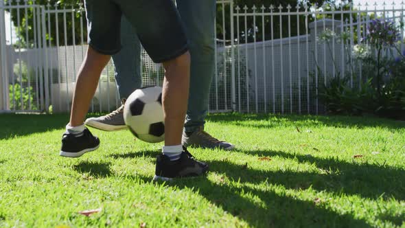 Midsection of biracial man and his son playing football in garden
