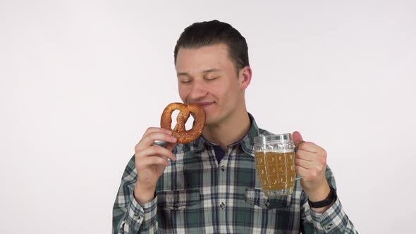 Cheerful Young Man Holding Mug of Beer Smelling Delicious Pretzel