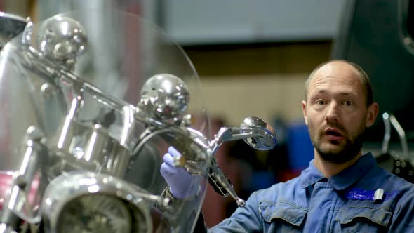 guy mechanic in blue overalls next to a motorcycle