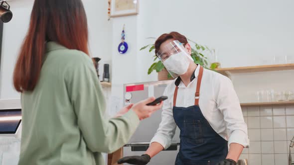 Asian customer people wear face mask, receive drink order from waiter on coffee bar counter in cafe.