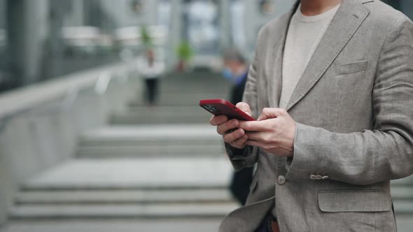Cropped View of the Caucasian Confident Young Businessman Using His Smartphone App Outside Near the