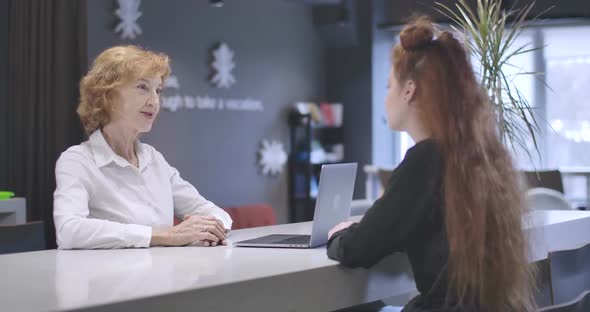 Portrait of Confident Middle Aged Office Worker Consulting Young Female Client in Open Space Office