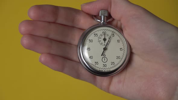 A woman's hand holds an analog stopwatch on a yellow background