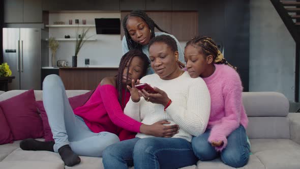 Joyful Black Family Networking and Sharing Cellphone on Couch