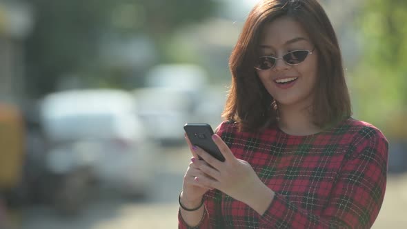 Happy Young Beautiful Asian Businesswoman Thinking While Using Phone Outdoors