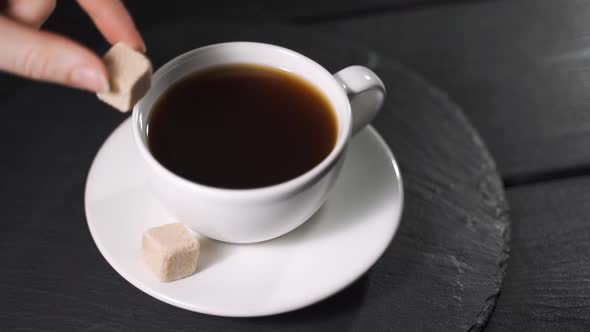 Close Up of a Woman Hand Throwing Sugar Cube Into a Coffee Mug on a Table at Home