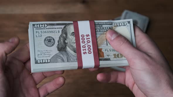 Stack of 10000 American Dollars Banknotes in Male Hands Over Wooden Background