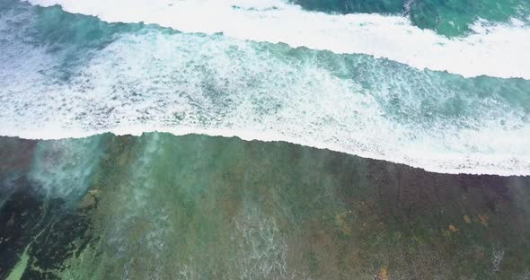 Aerial drone view of the surf and white waves breaking at the beach.