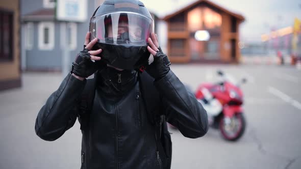 Biker puts on a helmet on the background of a motorcycle in the evening