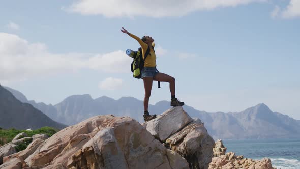 African american woman standing on rock with arms wide open while trekking in the mountains