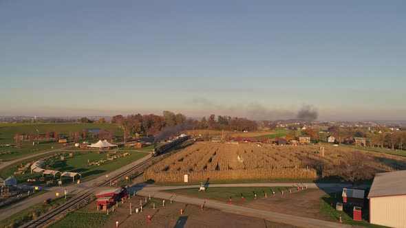 Aerial View of an Antique Steam Locomotive Approaching Pulling Passenger Cars and Blowing Smoke and Steam During the Golden Hour in late Afternoon