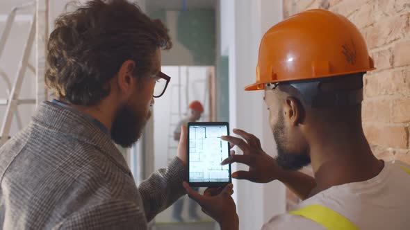 Back View of Apartment Owner and Foreman Discussing Blueprint on Digital Tablet