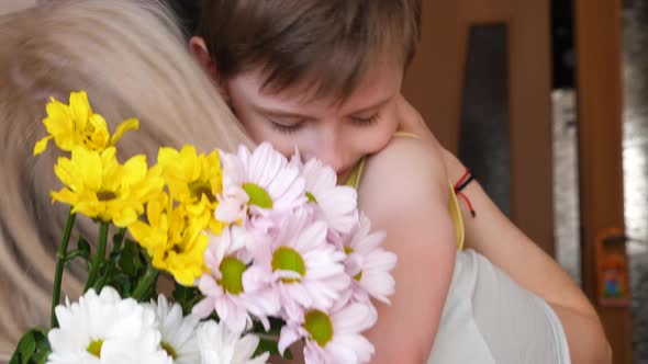  cute caucasian boy 7 years old with flowers hugs blonde mom, son gives mom a bouquet of white and y