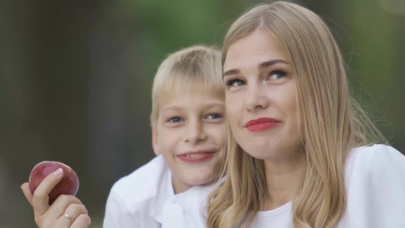 Attractive Blond Woman Sitting with Little Boy, Holding Apple in Hand and Talking