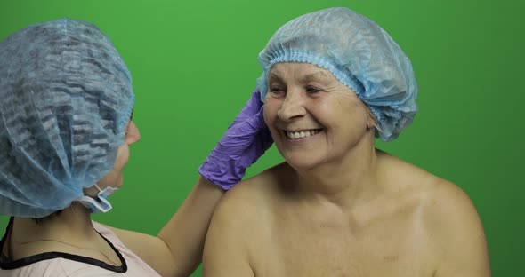 Smiling Elderly Female in Protective Hat. Plastic Surgeon Checking Woman Face