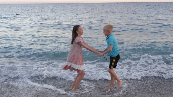 Little Brother and Sister Having Fun on the Beach They Hold Hands and Jump