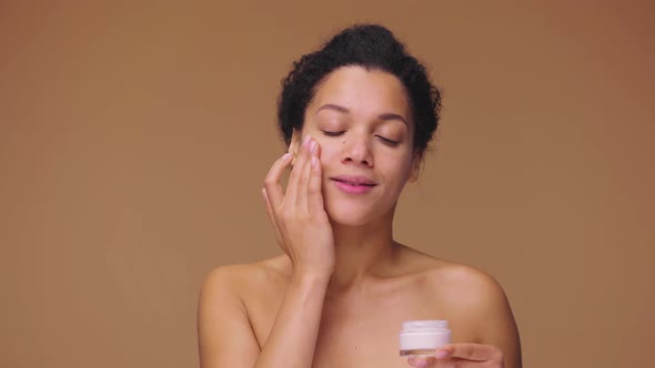 Beauty Portrait of Young African American Woman Applying Skincare Cream on Face