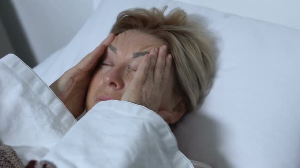 Elderly Woman Massaging Head in Bed